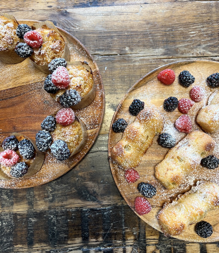 Golden muffins and mini cakes dusted with powdered sugar and garnished with berries sit on wooden plates