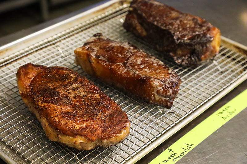 Three steaks resting on a wire rack.