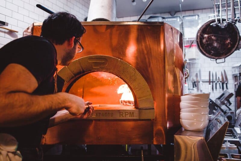 Matt Hyland putting pizza in brick wood-fired oven