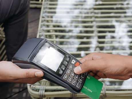 Close-up of a customer inserting a green credit card into a handheld payment terminal held by an employee.