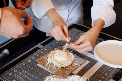 A chef skillfully uses a knife to slice a cake on a wooden cutting board in a well-lit kitchen.