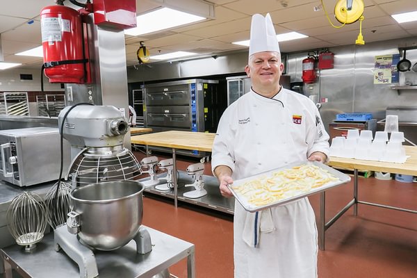 Chef Hervé stands smiling in a spacious commercial pastry kitchen at ICE's LA campus. 