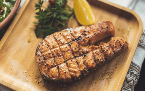 Grilled salmon fillet on a wooden tray accompanied by a fresh side salad.