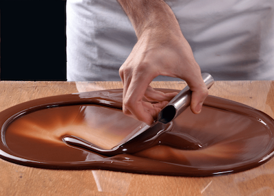 A person dips a chocolate bar into a bowl of rich chocolate sauce, showcasing a delicious dessert preparation.