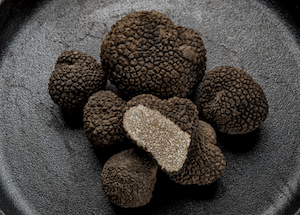 A plate displaying several whole black truffles, showcasing their rough, dark exterior.