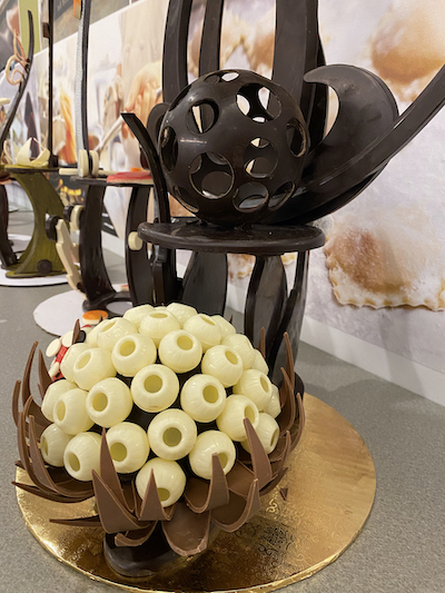 A chocolate sculpture with a spherical design, featuring intricate hollowed dark chocolate and white chocolate spheres on a gold base, exuding elegance.