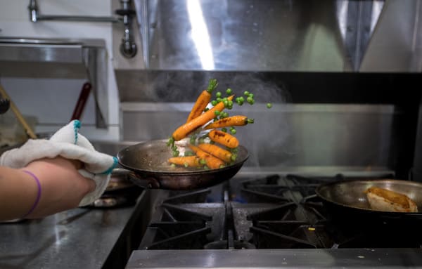 chef flipping carrots in saucepan