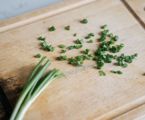 Chopped green onions scattered on a wooden cutting board, with whole green onions on the side.