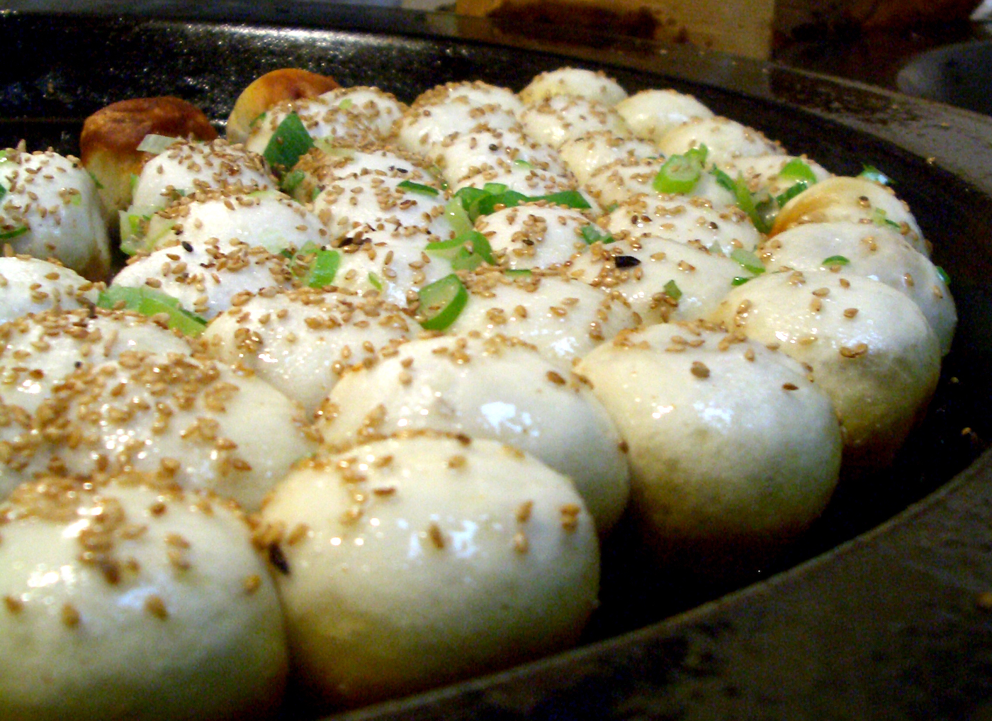 Multiple shen jiao bao, one of the types of Chinese dumplings, being cooked in a pan