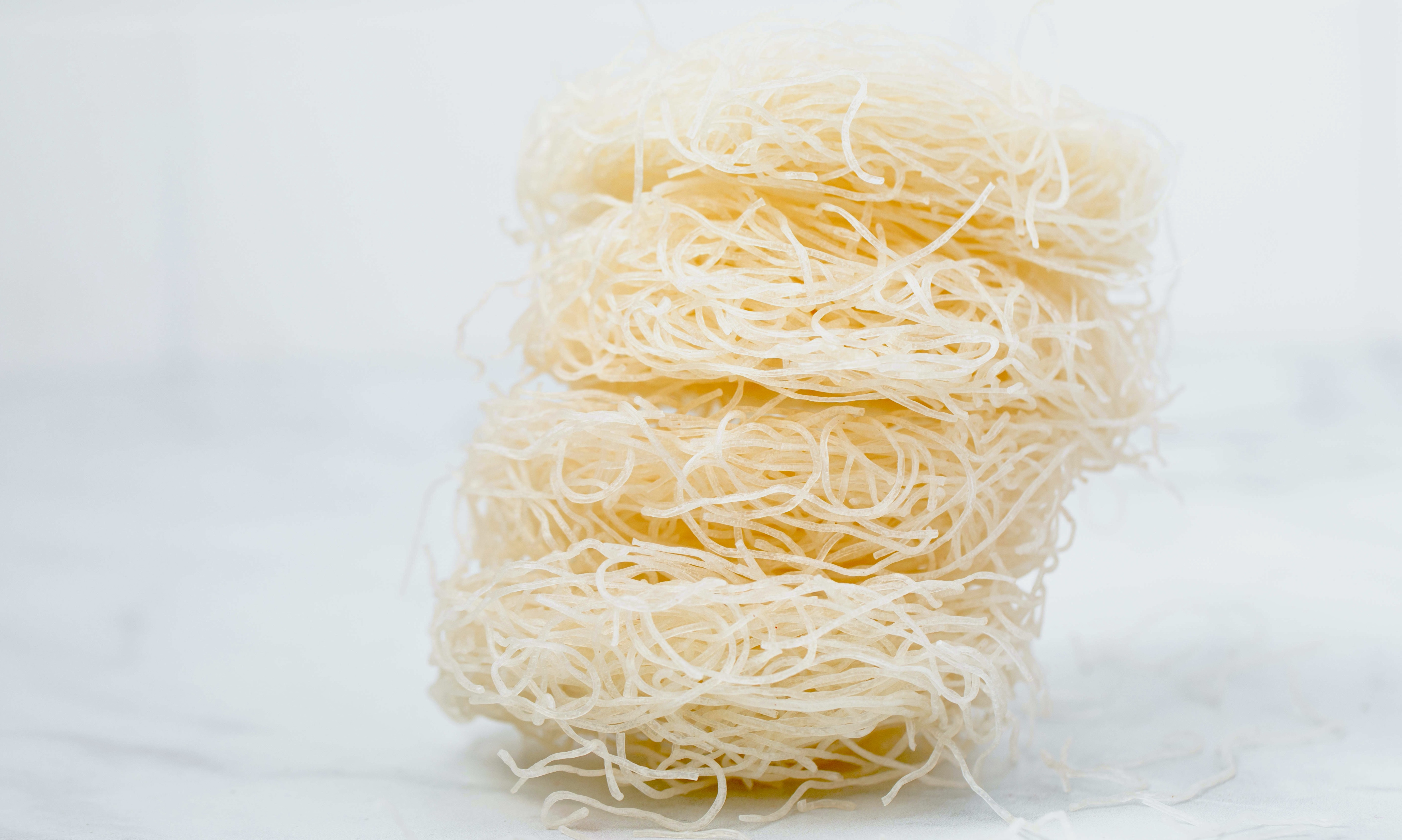 Uncooked rice noodles sit in front of a white background
