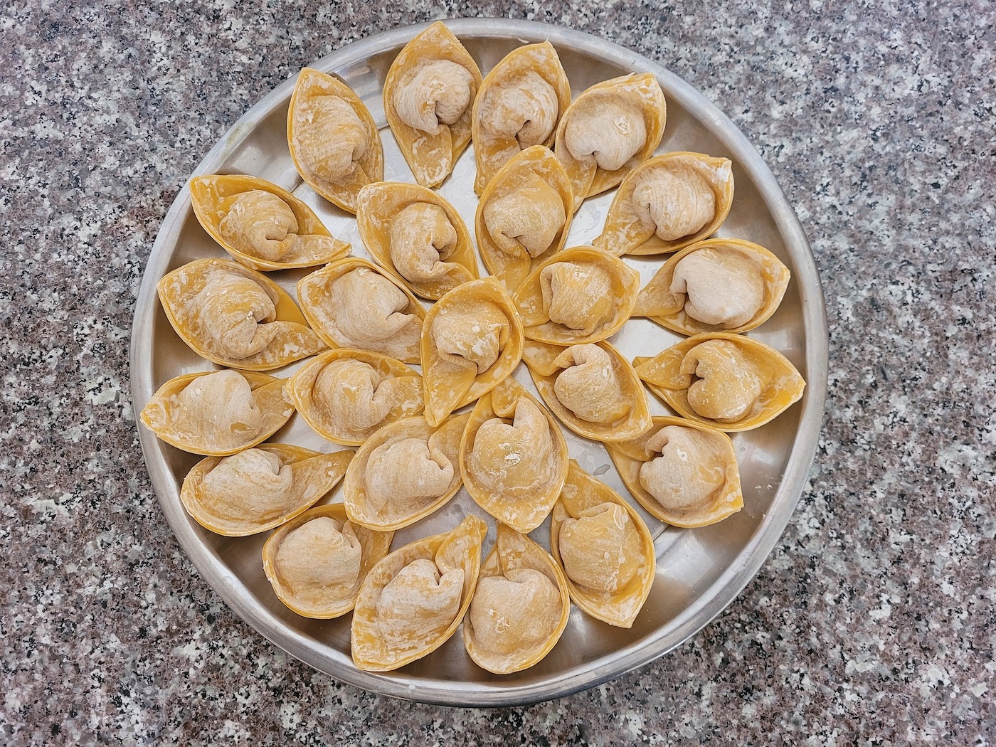 Uncooked wontons, one of the types of Chinese dumplings, sit on a metal tray