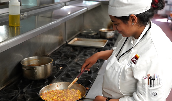 An ICE student cooks a dish in a pan on a stove for the plant based associate degree program