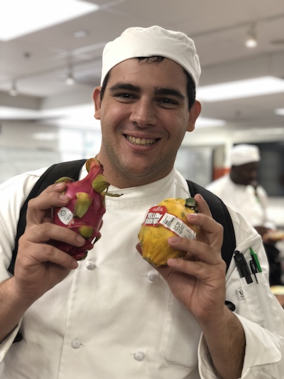 Adriano holds up fruit as a student at ICE