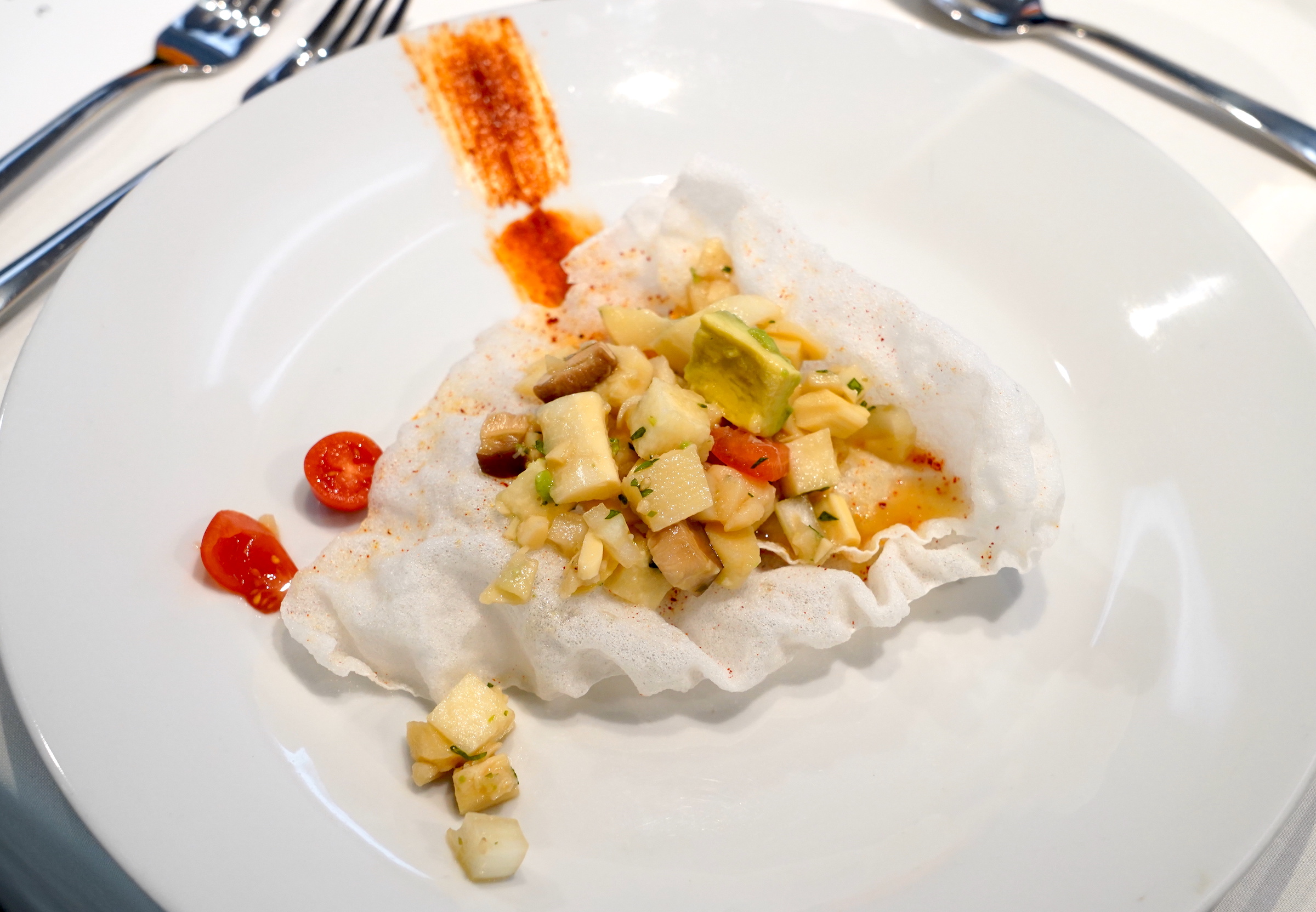 Plant-based ceviche on a rice cracker sits on a white plate