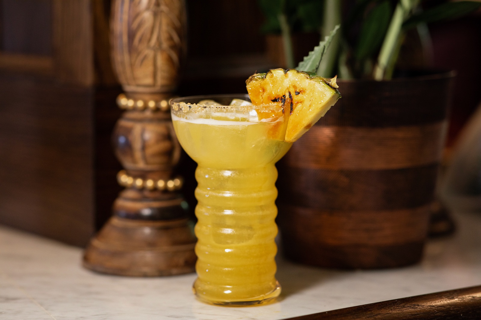 A yellow drink with a slide of charred pineapple sits on a counter