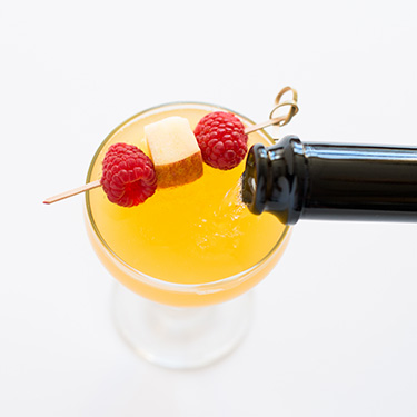 A bottle of champagne pours into a glass with a speared garnish on top