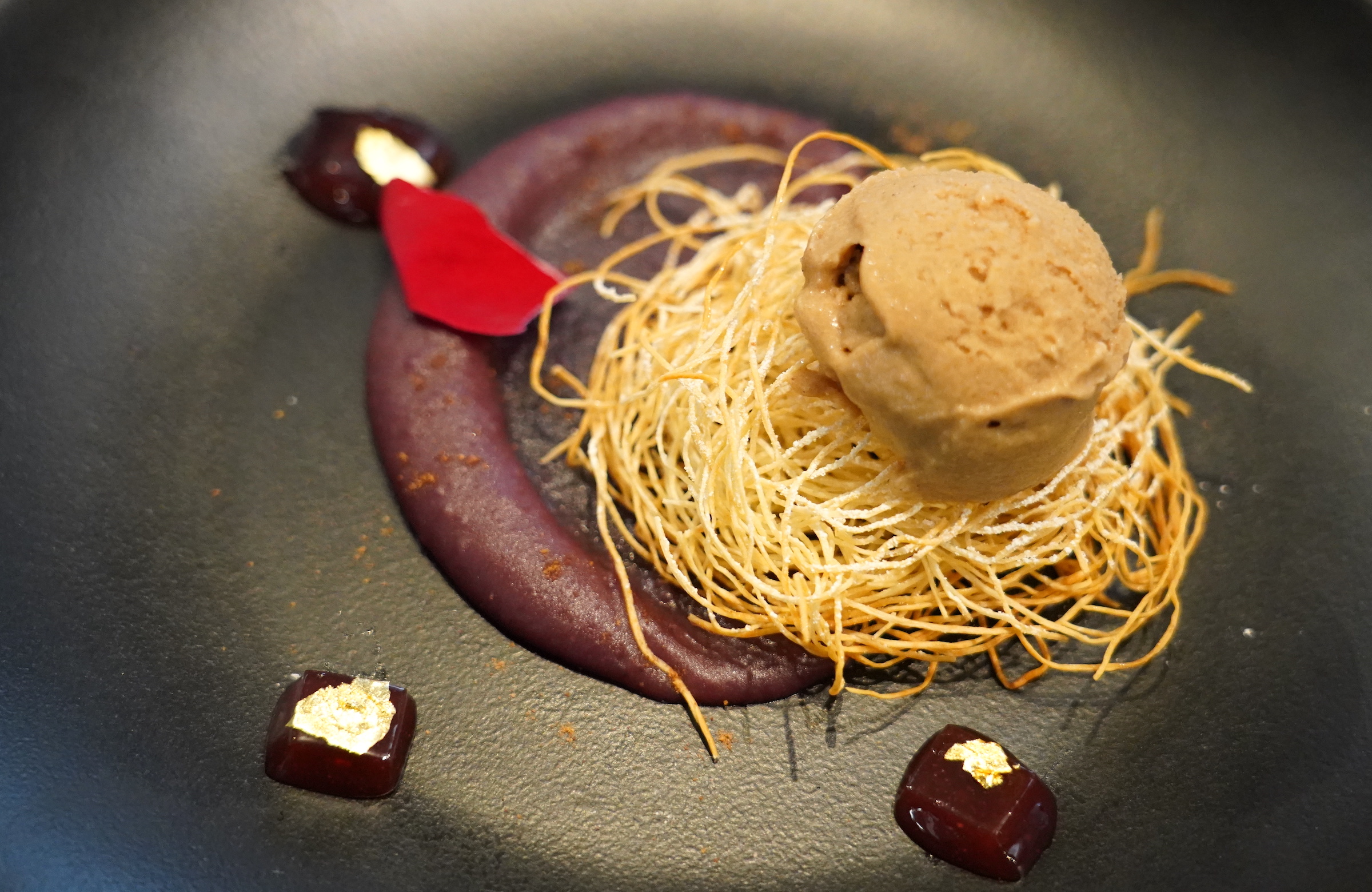 Plant-based ice cream and phyllo dough on top of purple sweet potato puree sit on a black plate