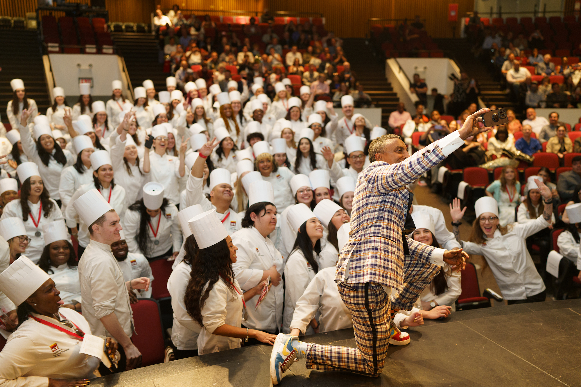 Marcus Samuelsson takes a selfie from stage with ICE graduates at ICE New York's 2023 commencement ceremony