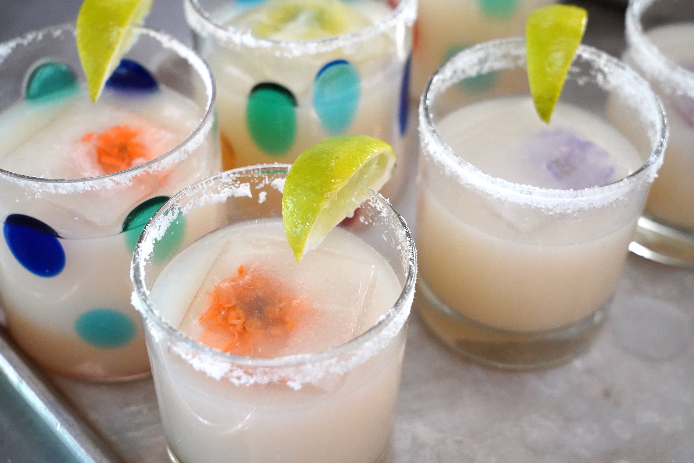 Non-alcoholic lychee margaritas in multi-colored glasses sit on a metal tray