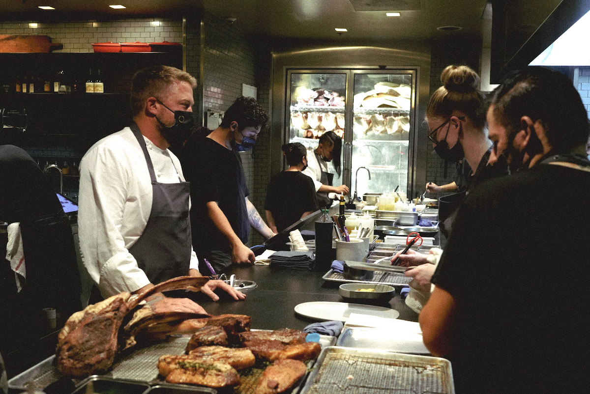ICE alumni in black shirts and blue aprons work the kitchen line at Otium restaurant in Los Angeles