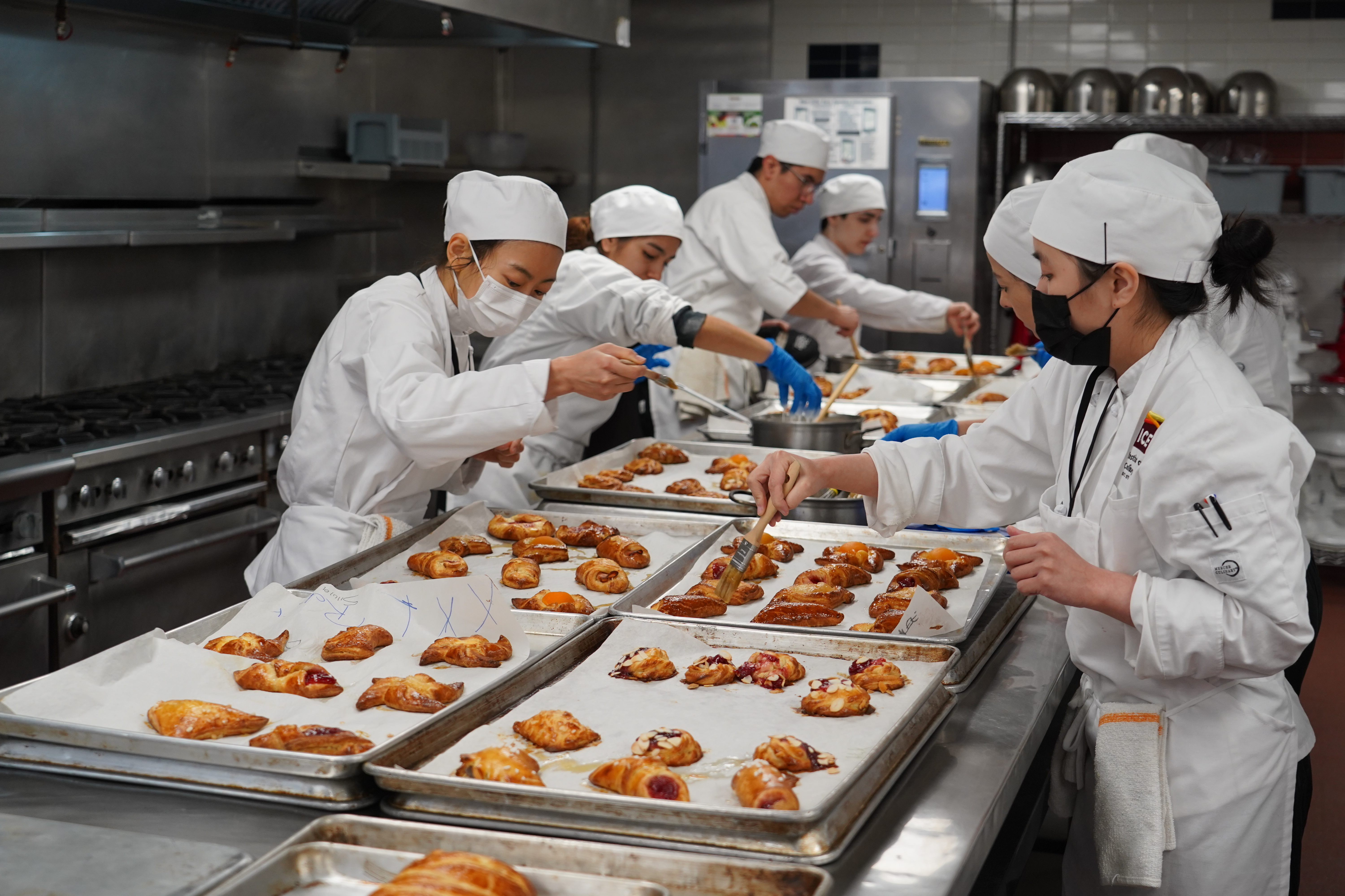 ICE Pastry & Baking students in white coats work together to glaze sheets of pastries