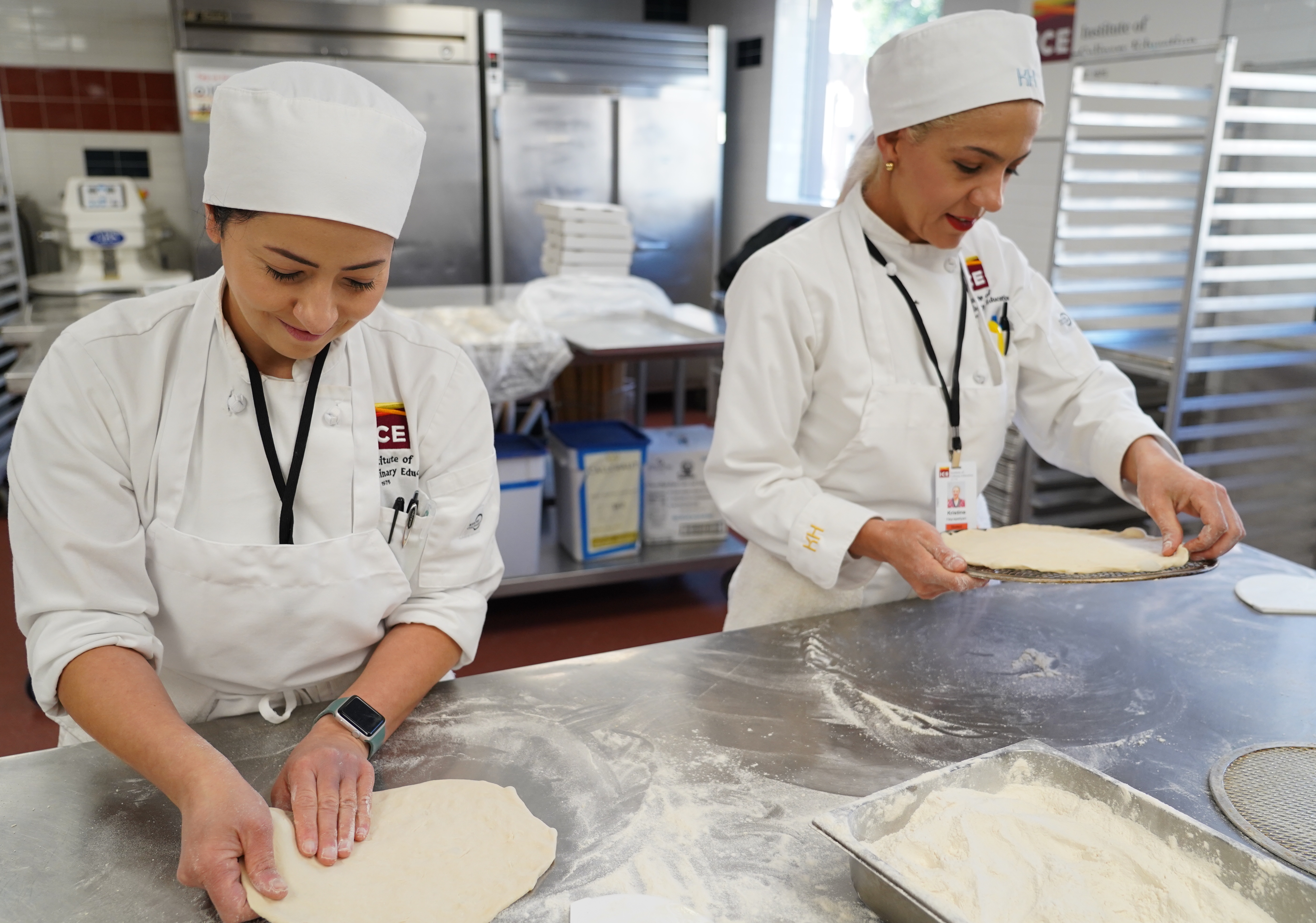Two ICE students shape pizza dough on a metal table
