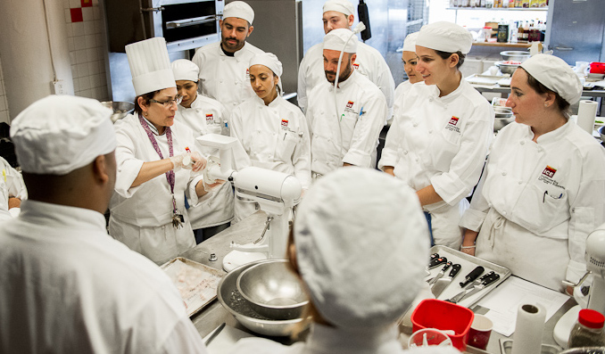 A group of students gather around a chef-instructor