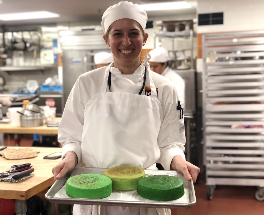 A student prepares three cake layers with varying shades of green