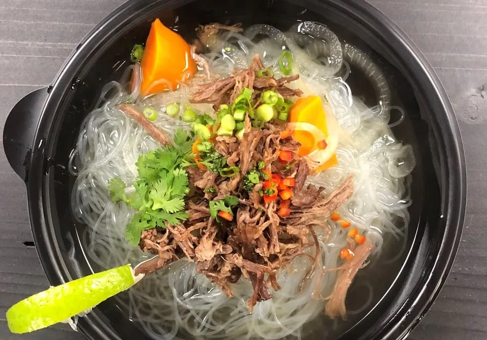Pho noodle soup with beef, herbs and scallions in a black bowl with a green spoon