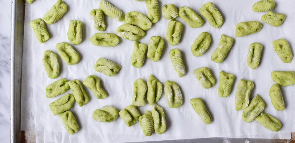 Green gnocchi spread out on a sheet pan.