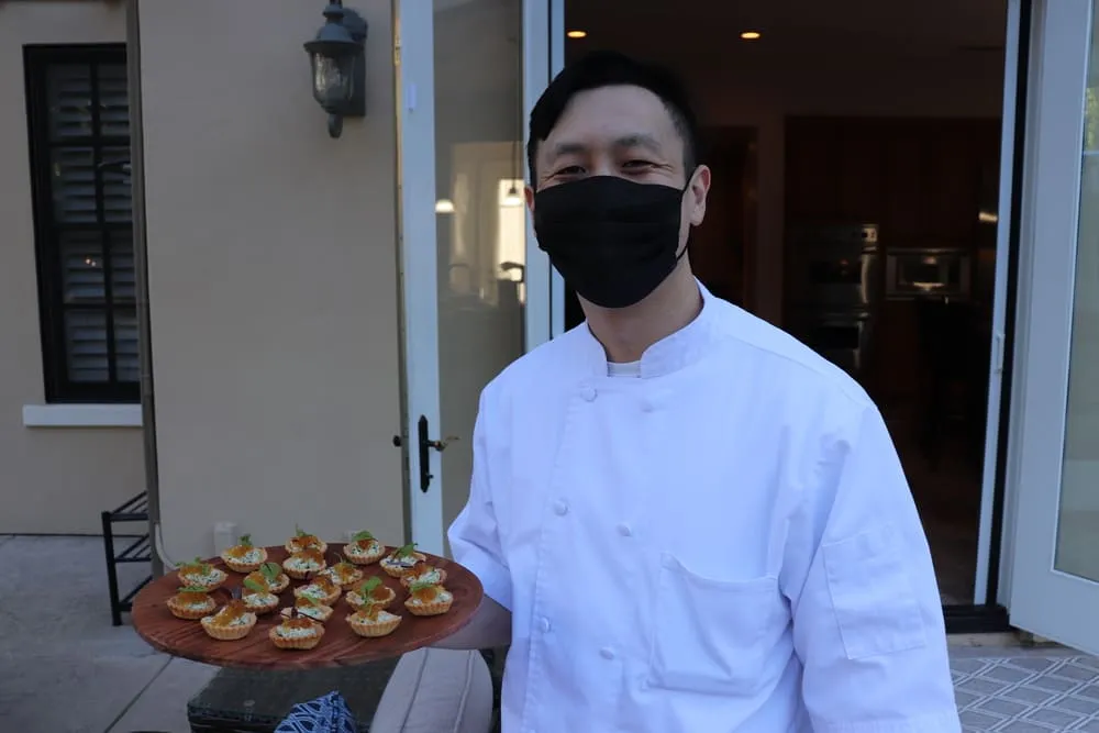 Sous Chef Keita Suzuki in chef whites holds a platter of small bites.