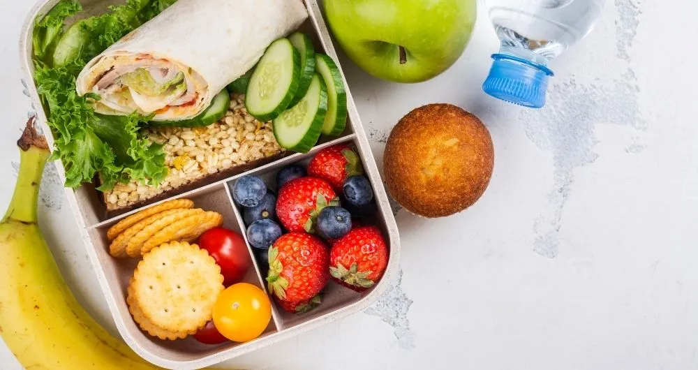 An overhead view of a healthy lunch box meal layout on a light textured background.