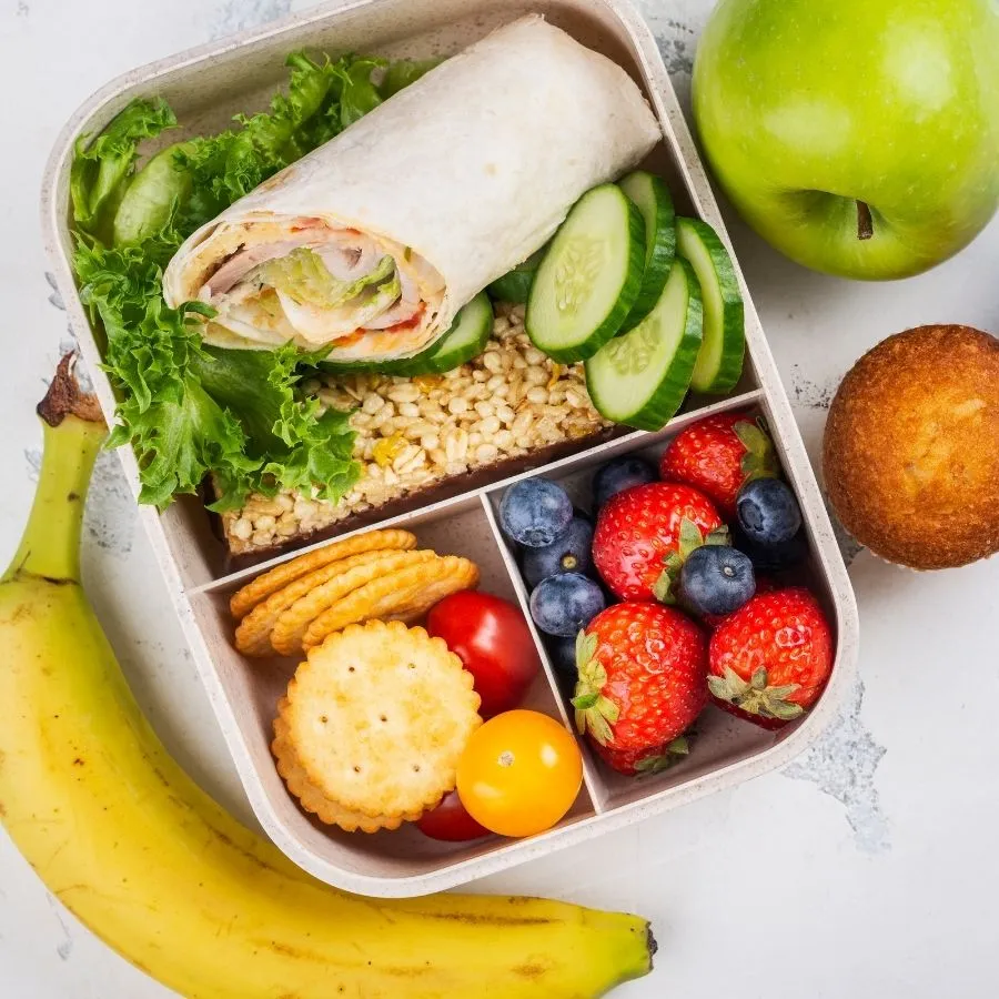 An overhead view of a healthy lunch box meal layout on a light textured background.
