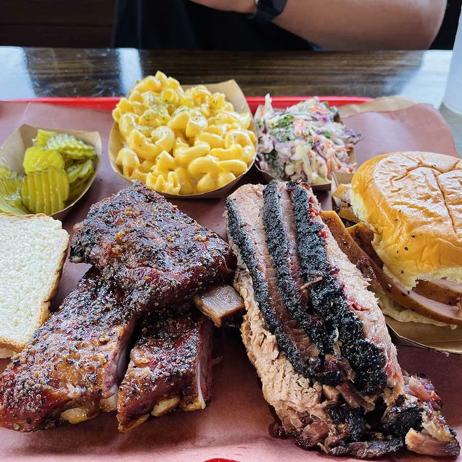 A plate of barbecued meats, bread, coleslaw, pickles and mac and cheese