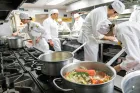 A bustling Institute of Culinary Education (ICE) commercial kitchen filled with students wearing white chef uniforms and matching caps.