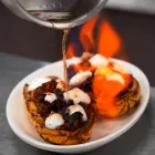 A pot of flaming liquid pours onto a stuffed squash on a white plate