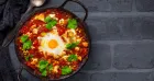 . A skillet with a sunny-side-up egg surrounded by vibrant tomato sauce on a rustic table.