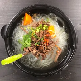 Pho noodle soup with beef, herbs and scallions in a black bowl with a green spoon