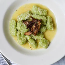 Green gnocci on white plate topped with sauteed oyster mushrooms.