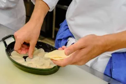 Chef hands layer thin potato slices in a cast iron oval roaster to make scalloped potatoes.