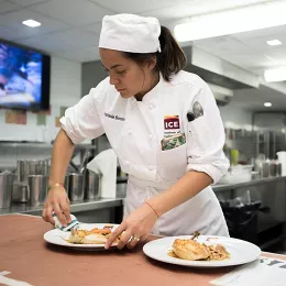 An ICE culinary arts student finishes plating a dish during mock restaurant service at culinary school