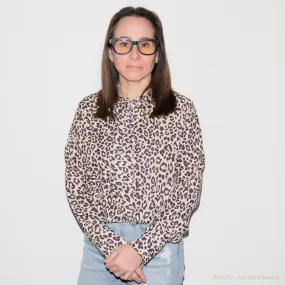 Rebecca Roth Gullo in an animal print top and ripped blue jeans in front of a beige wall.
