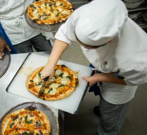 Chef cutting fresh homemade pizza in professional kitchen in New York
