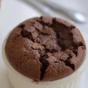 Two chocolate souffles in white ramekins sit on a white plate