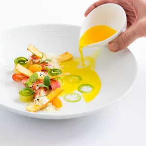 a chef pours sauce onto a plated dish