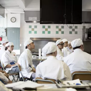 Culinary students in New York City sitting and listening to a lesson from their instructor