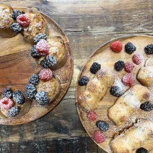 Muffins and mini cakes dusted with powdered sugar and garnished with berries sit on wooden plates