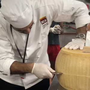 An ICE student learns how to open a wheel of Parmigiano-Reggiano.
