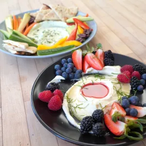 Two plates of whipped feta dip with vegetables and cut fruit