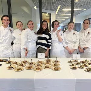 Chef Adrienne Cheatham stands with a group of ICE students behind a table of small plated dishes